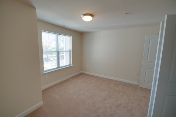 A spacious, empty room with a carpeted floor and a large window letting in natural light.