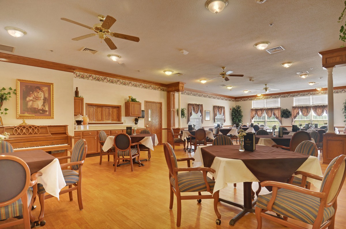 A spacious dining area with neatly arranged tables and chairs, featuring ceiling fans and wooden flooring.