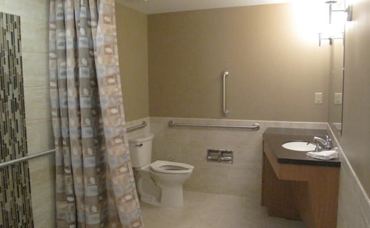 A bathroom with accessible features, including a toilet, sink, and grab bars next to the shower area.