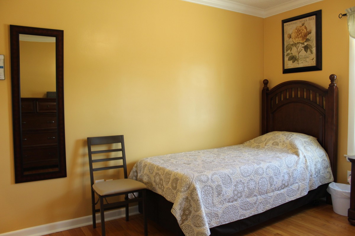 A minimalist bedroom with a single bed, chair, and yellow walls.