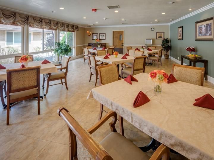 A well-lit dining area with neatly arranged tables and chairs, featuring elegant table settings with red napkins.