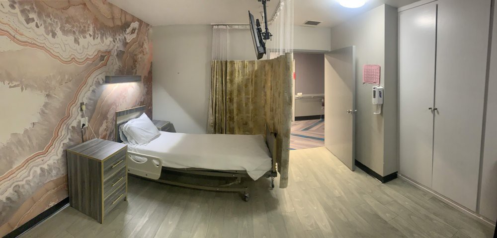 A hospital room with a single bed, television, and privacy curtain.
