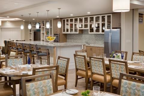 A modern kitchen and dining area featuring a bar counter with pendant lights, surrounded by wooden chairs and tables.