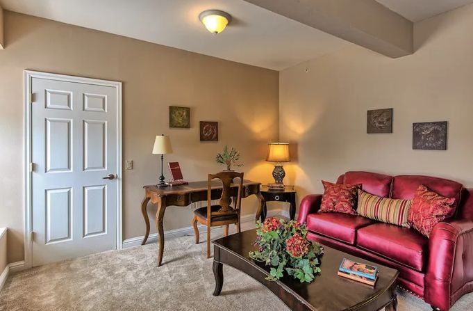 A cozy living room with a red sofa, wooden desk, and warm lighting.