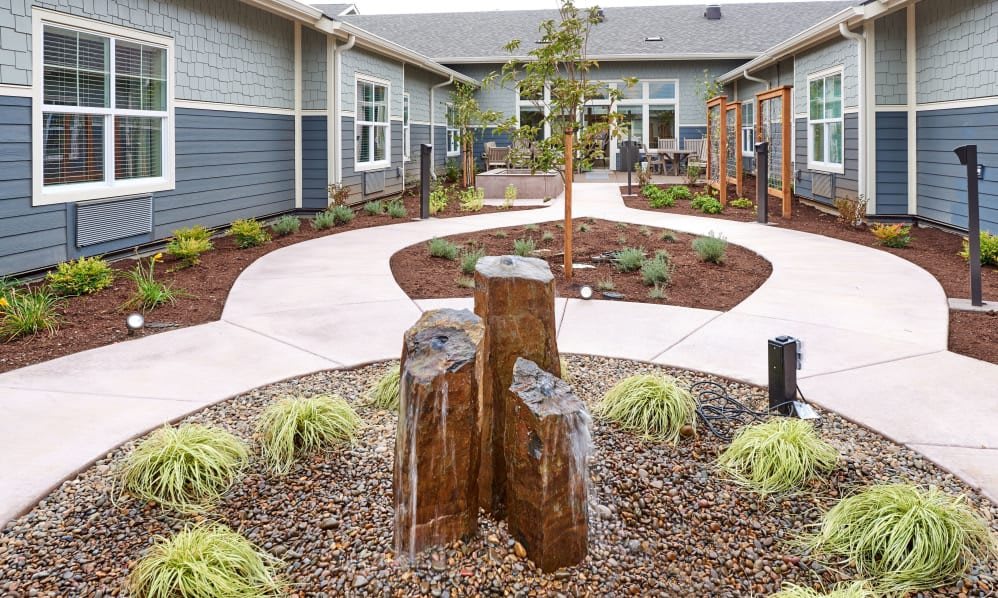 A landscaped courtyard with a winding pathway, surrounded by plants and modern architecture.
