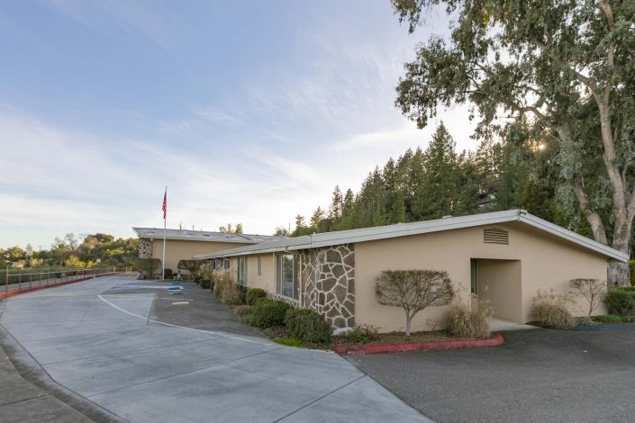 A roadside motel with a parking area surrounded by trees and a clear sky.