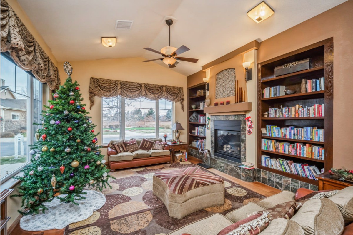 A cozy living room decorated for Christmas with a tree, fireplace, and bookshelves.