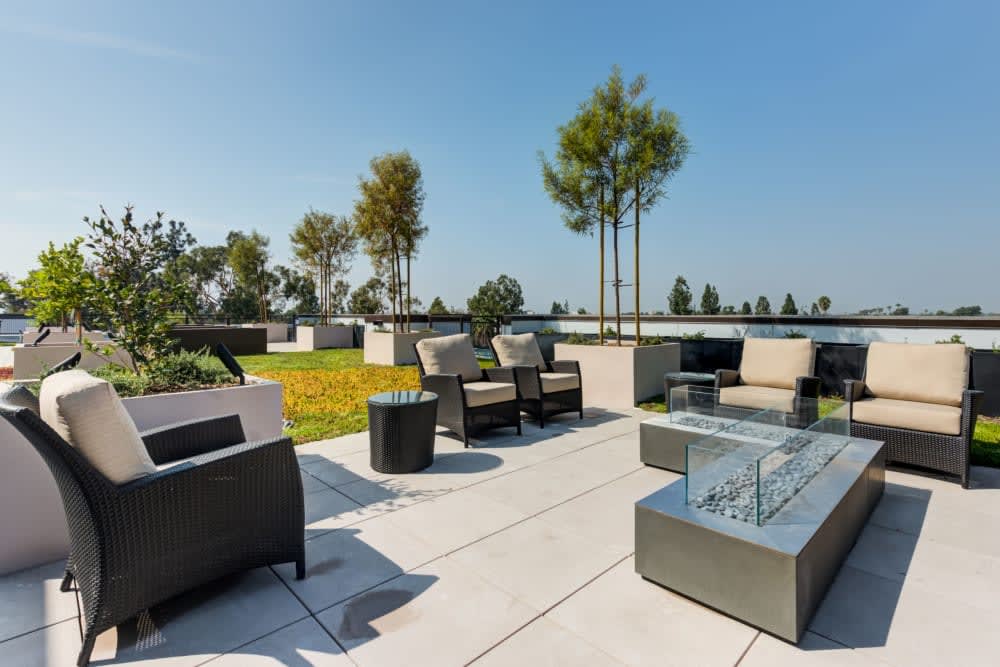 Modern outdoor patio area with comfortable seating and a fire pit surrounded by trees.