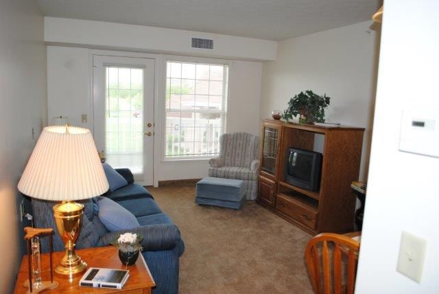 A cozy living room featuring a sofa, armchair, television on a wooden stand, and a large window.