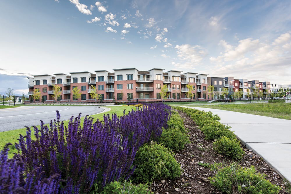 Modern apartment complex with vibrant landscaping and a clear sky backdrop.