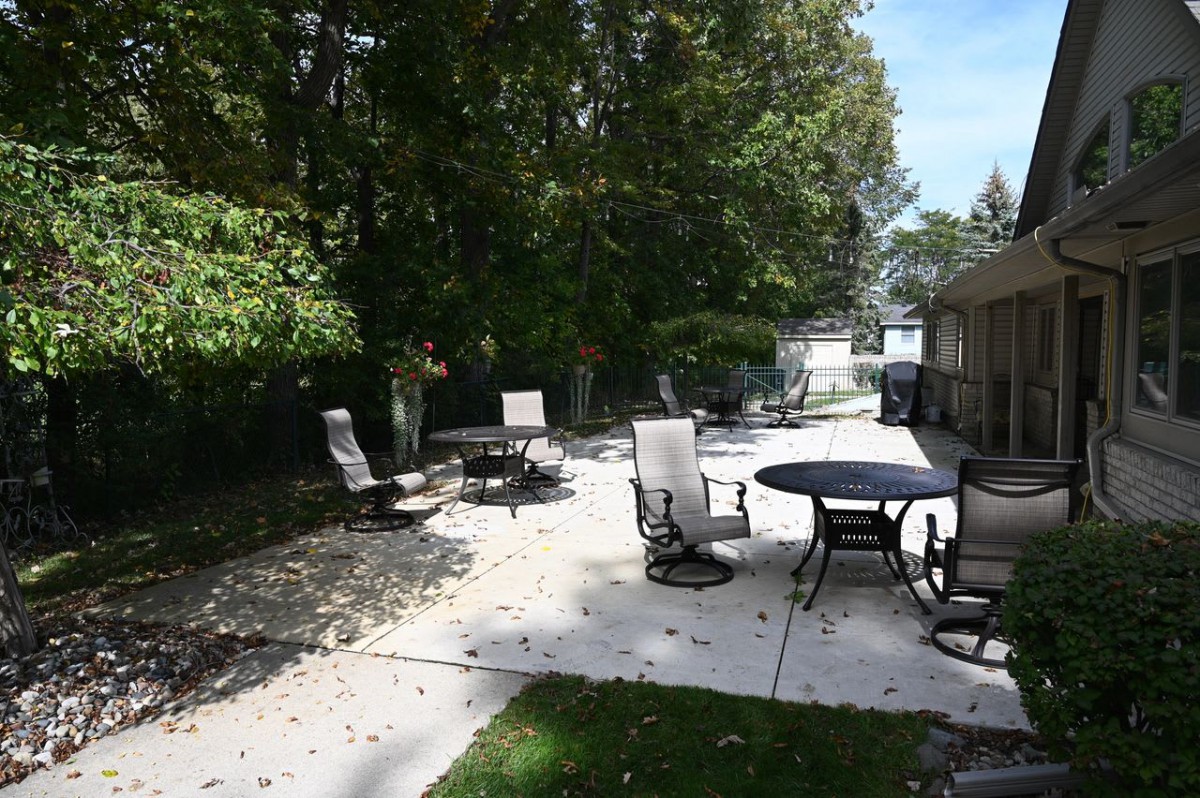 A peaceful backyard patio with chairs and tables under the shade of trees.