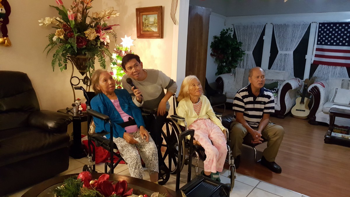 A family gathering in a warmly decorated living room with elderly members seated in wheelchairs.