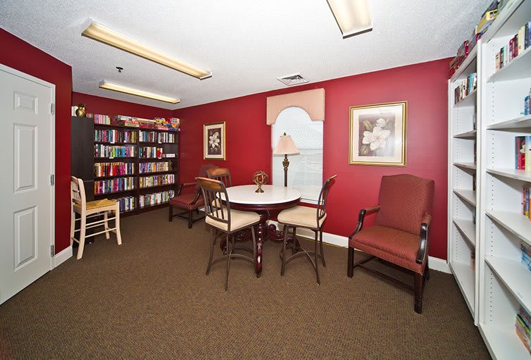 A cozy reading room with red walls, featuring bookshelves, a round table surrounded by chairs, and decorative artwork.
