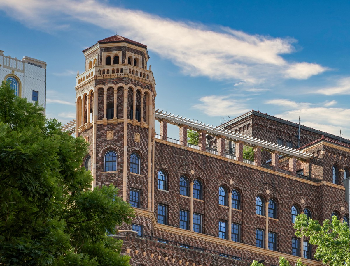 A historical brick building with a tower and arched windows surrounded by greenery.