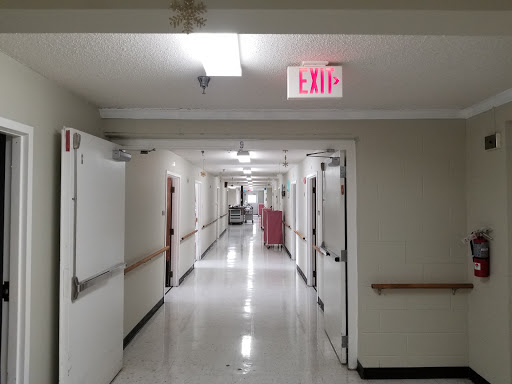 A long, empty hallway in a hospital, featuring exit signs and closed doors.