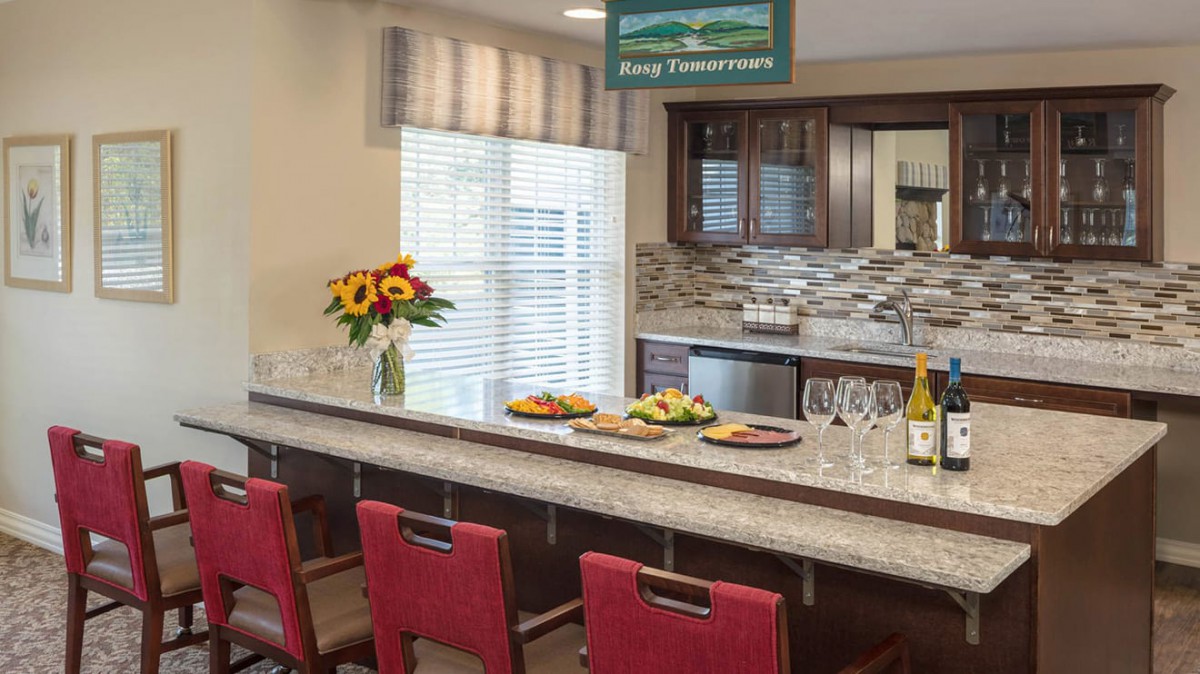 A modern kitchen with a long countertop, red chairs, and decorative elements like flowers and food.