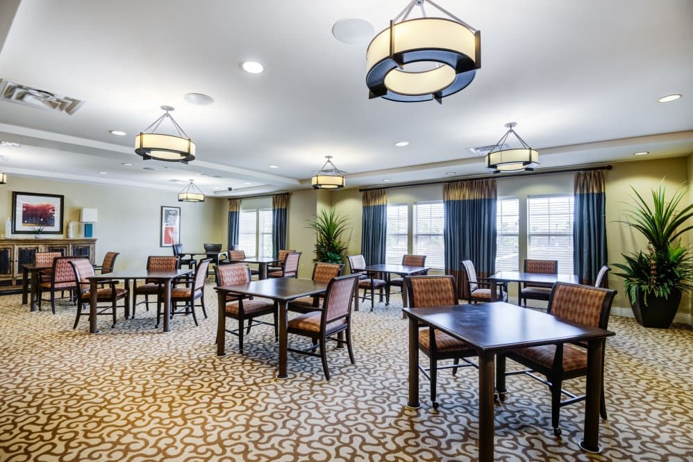 A well-lit dining area with multiple tables and chairs arranged on a patterned carpet.