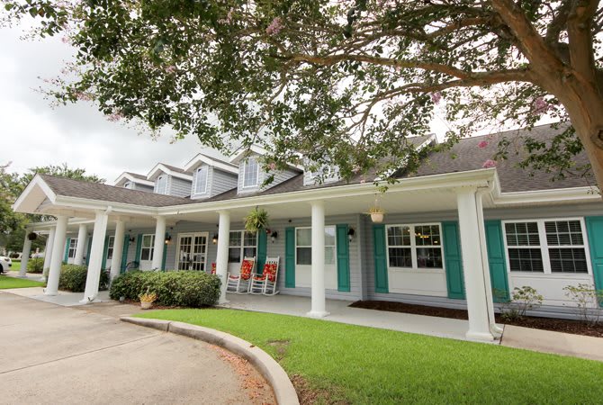 A charming house with a spacious porch and teal shutters set amidst green lawns and trees.