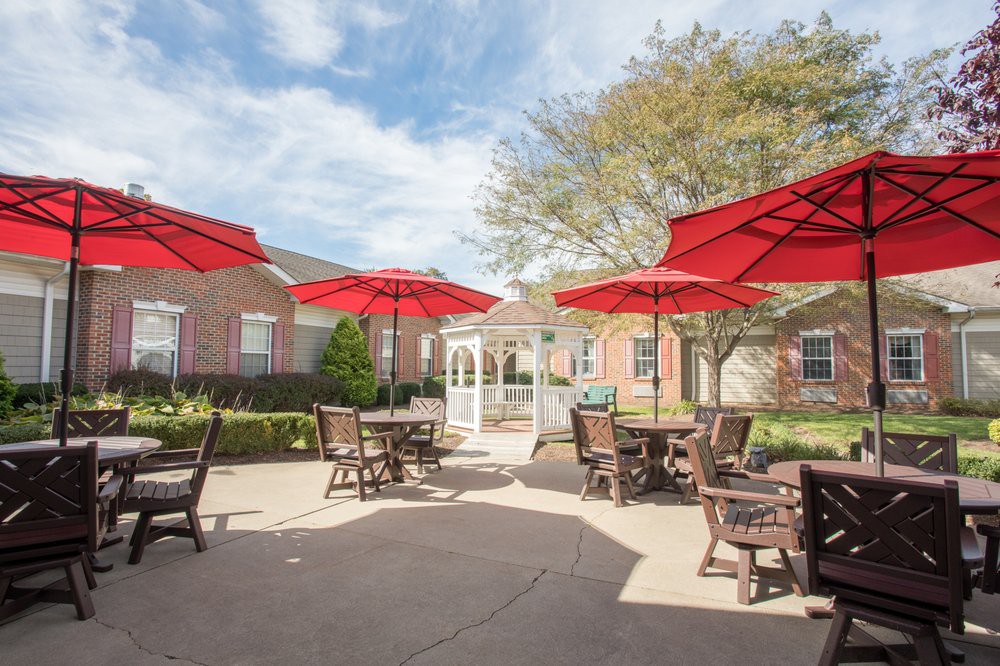 A sunny outdoor patio with tables and red umbrellas in front of a brick building.
