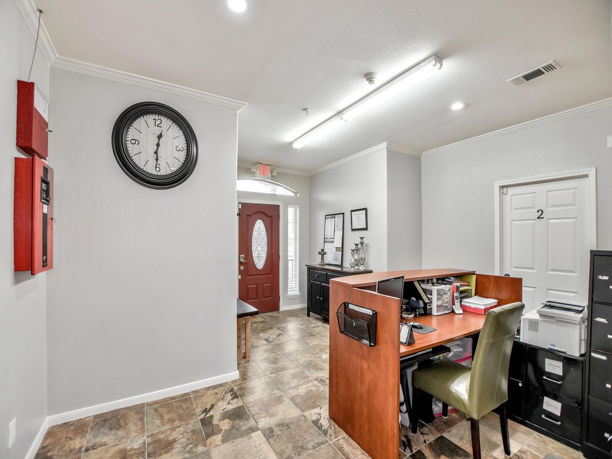 An office reception area with a desk, chairs, and a wall clock.
