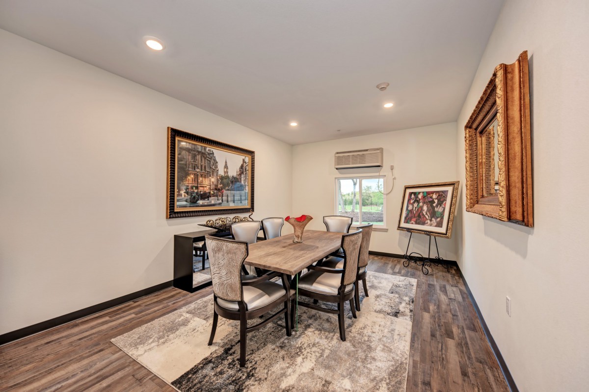 A well-furnished dining room featuring a wooden table with upholstered chairs, artwork on the walls, and a large window allowing natural light to fill the space.