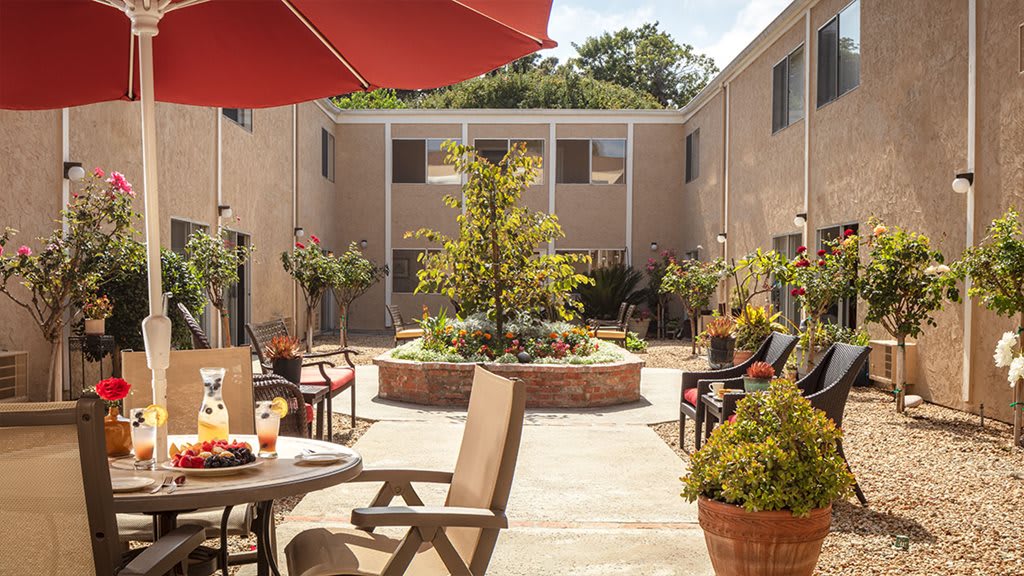 A sunny courtyard with patio furniture and lush greenery in an apartment complex.