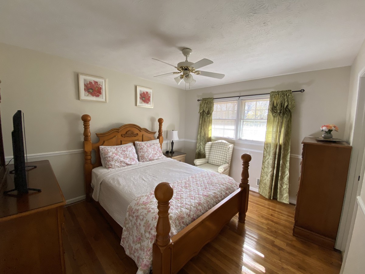 A cozy bedroom with a wooden double bed, ceiling fan, and decorative elements.