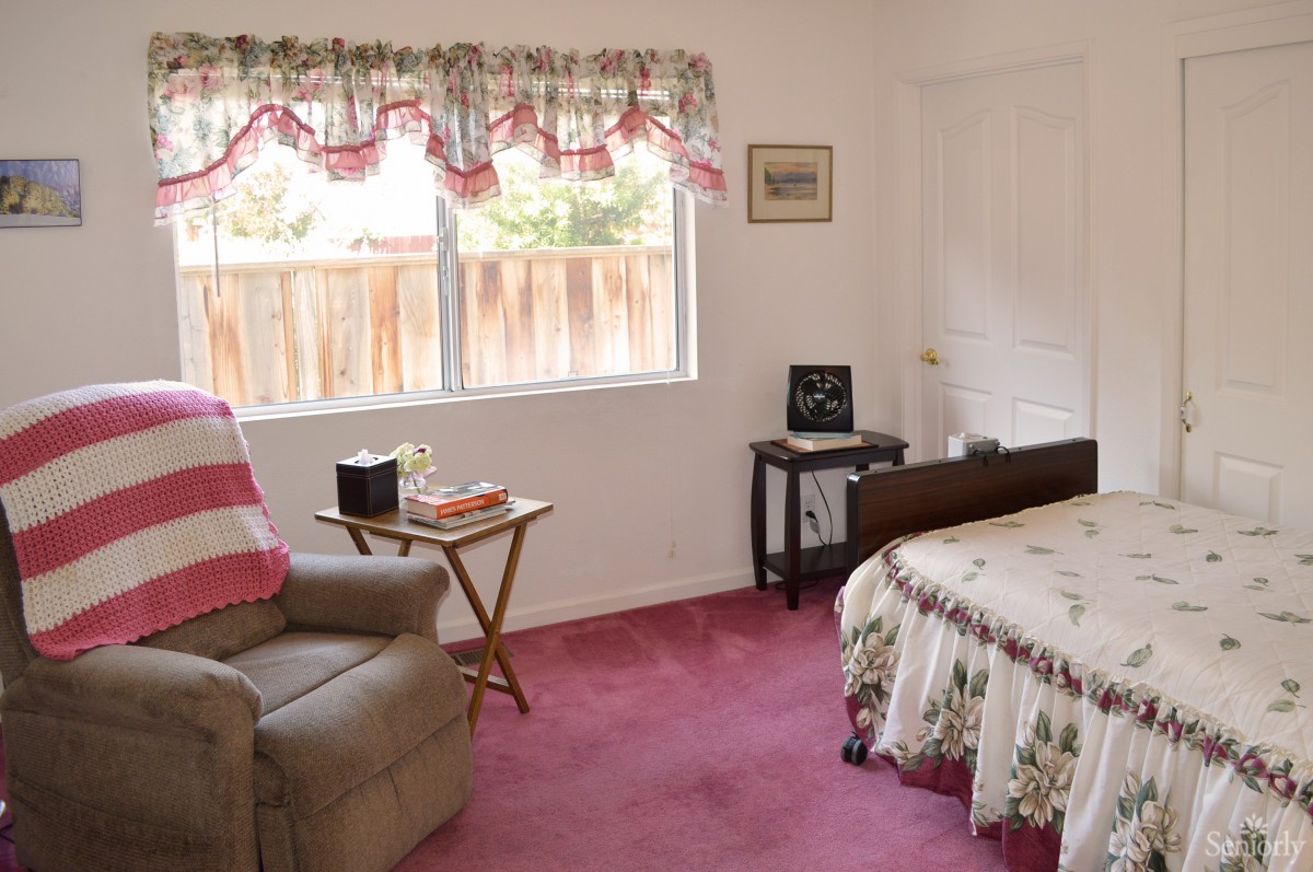 A cozy bedroom with a floral bedspread and an armchair next to a window.
