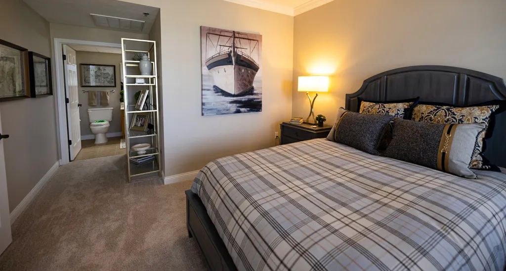 A cozy bedroom with plaid bedding and a ship painting on the wall.
