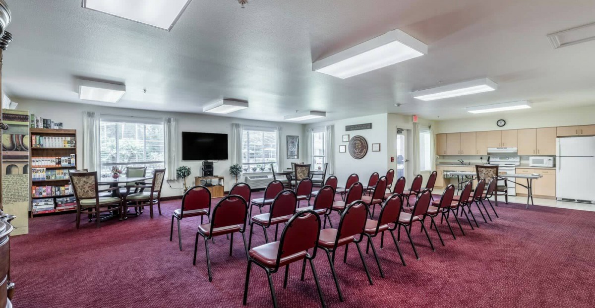 A well-arranged conference room with rows of red chairs facing a television.