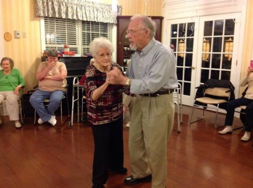 An elderly couple dances together indoors, enjoying a social activity.