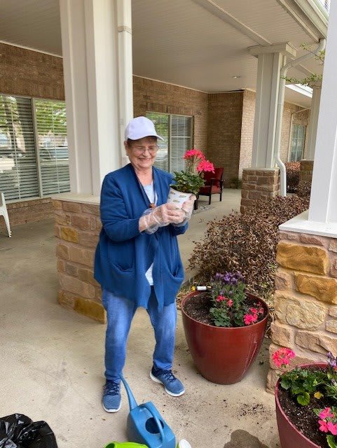 A woman holding a potted plant while smiling outdoors.