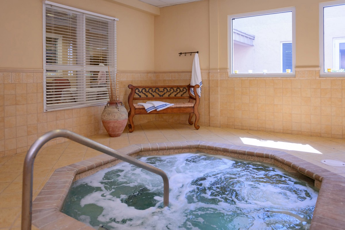 An inviting indoor hot tub area with bubbling water, a wooden bench, and large windows.