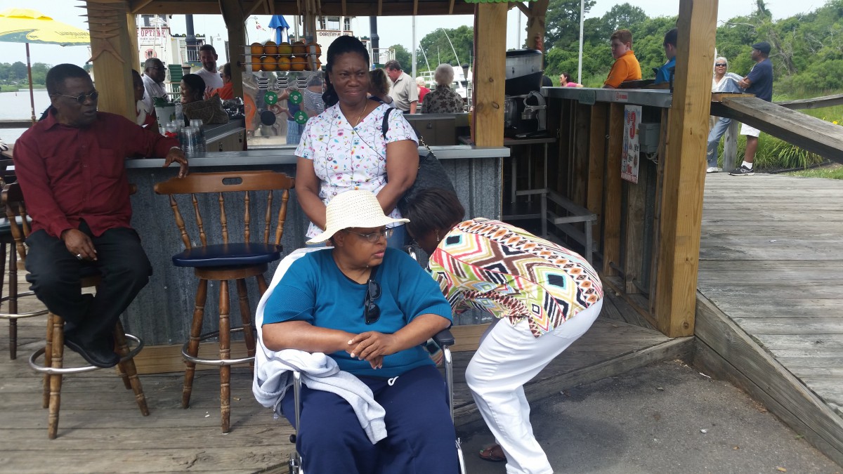 A group of people enjoying a day outdoors, including one sitting in a wheelchair wearing a hat.