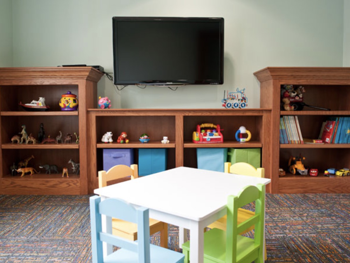 A cozy children's playroom with a small table and colorful chairs, surrounded by bookshelves filled with toys.