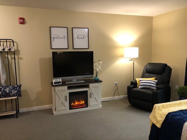 Cozy living room with a television set atop a fireplace, an armchair, and warm lighting.
