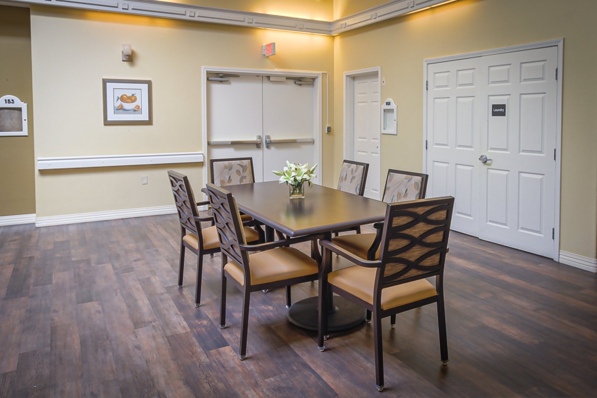 A dining area with a wooden table and six chairs set on a wood floor, surrounded by light-colored walls.