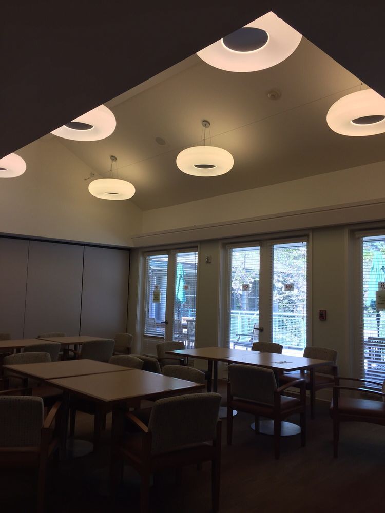 A well-lit dining area with tables and chairs, featuring large windows and modern lighting fixtures.