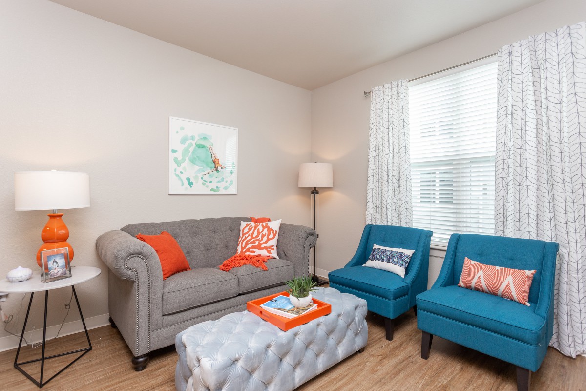 A cozy living room with a gray sofa, two blue armchairs, and bright orange accents.