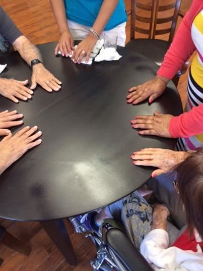 A group of people place their hands on a round table, suggesting a gathering or meeting.