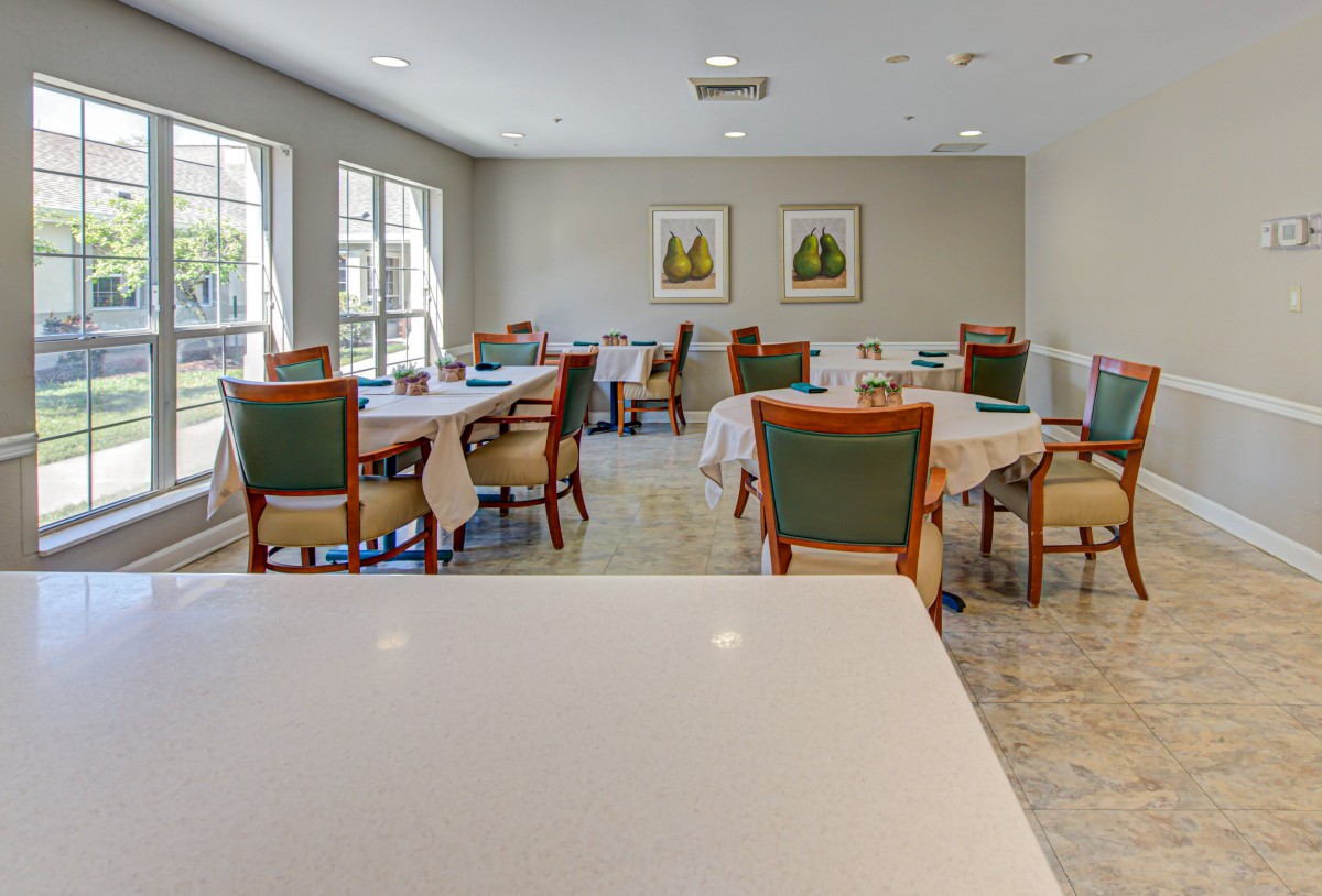 A bright and spacious dining room with neatly arranged tables and chairs, featuring large windows and wall artwork.