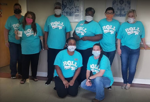 A dedicated team wearing teal 'ROLL' shirts and masks, gathered together indoors.