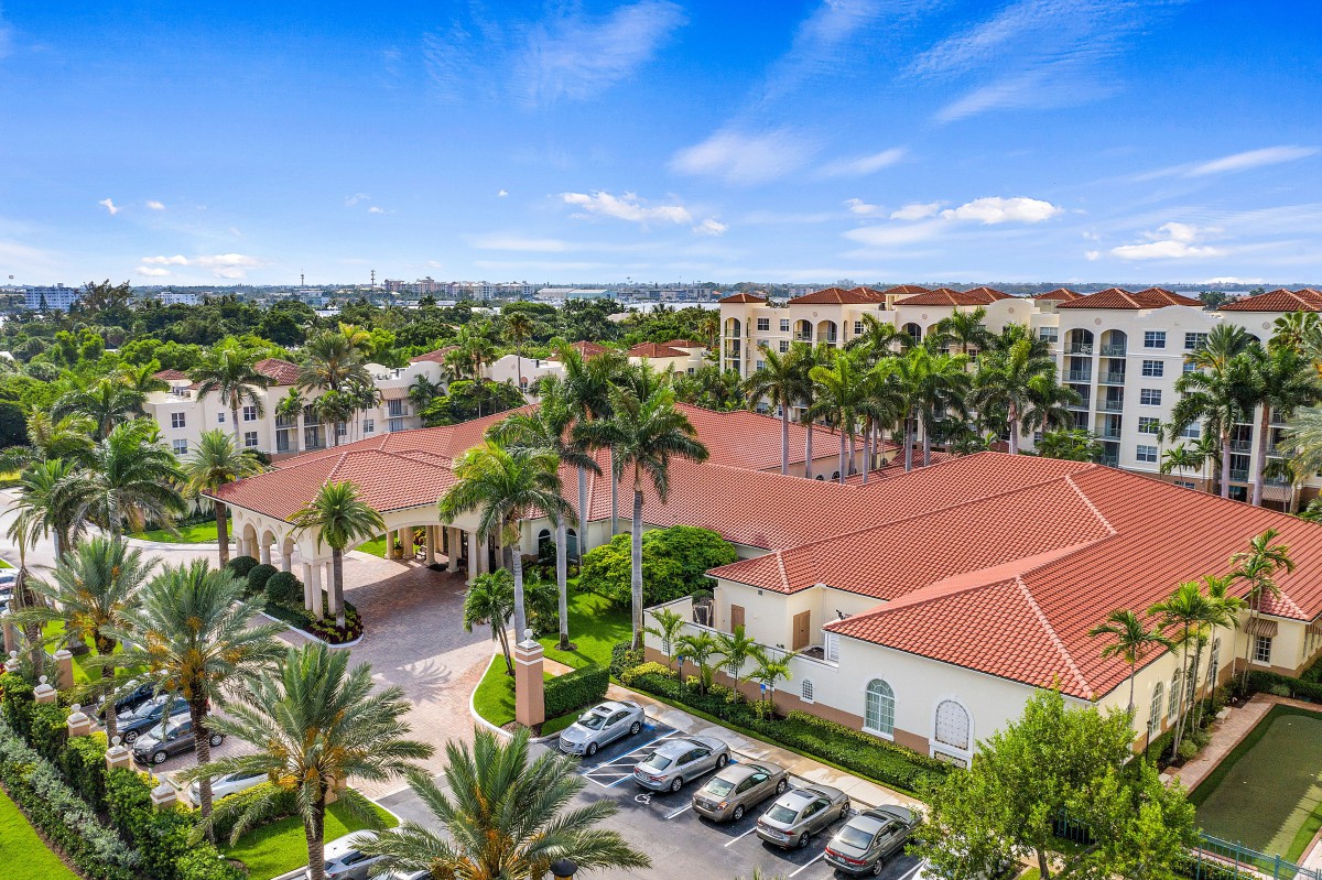 Aerial view of a residential area with red-roofed buildings surrounded by palm trees on a sunny day.