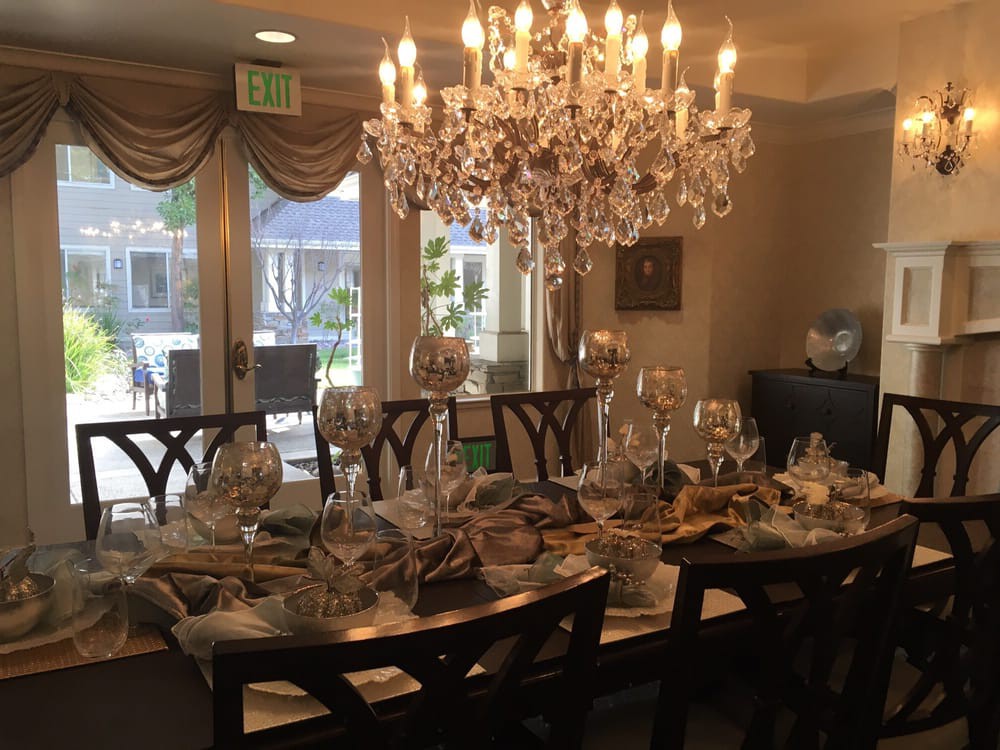 An elegantly set dining room with a sparkling chandelier and neatly arranged table settings.