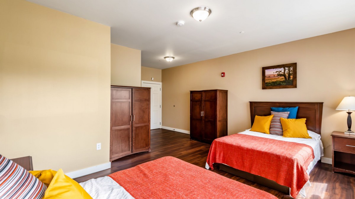 A simple bedroom featuring two beds with orange bedding and wooden furniture.