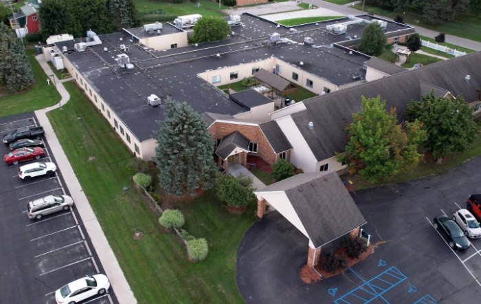Aerial view of a building with surrounding greenery and a parking area.
