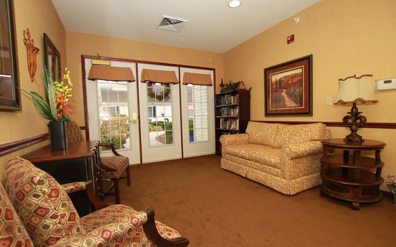 A cozy living room with a sofa, armchair, bookshelf, and glass doors leading outside.