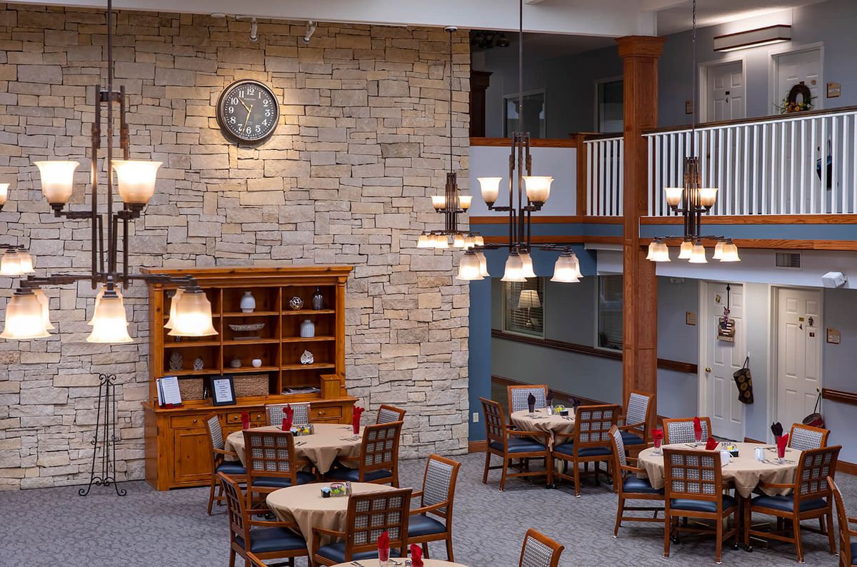 A cozy restaurant dining area with round tables, wooden chairs, a stone wall, and elegant chandeliers.