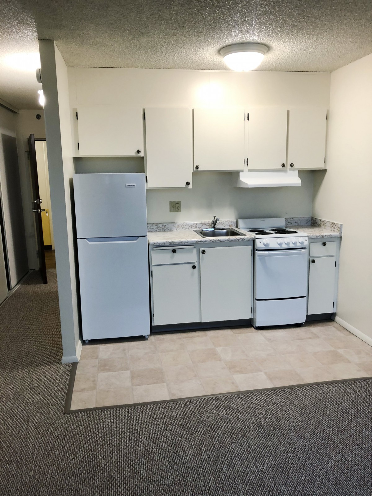 A compact kitchen setup in an apartment with a refrigerator, oven, and sink.