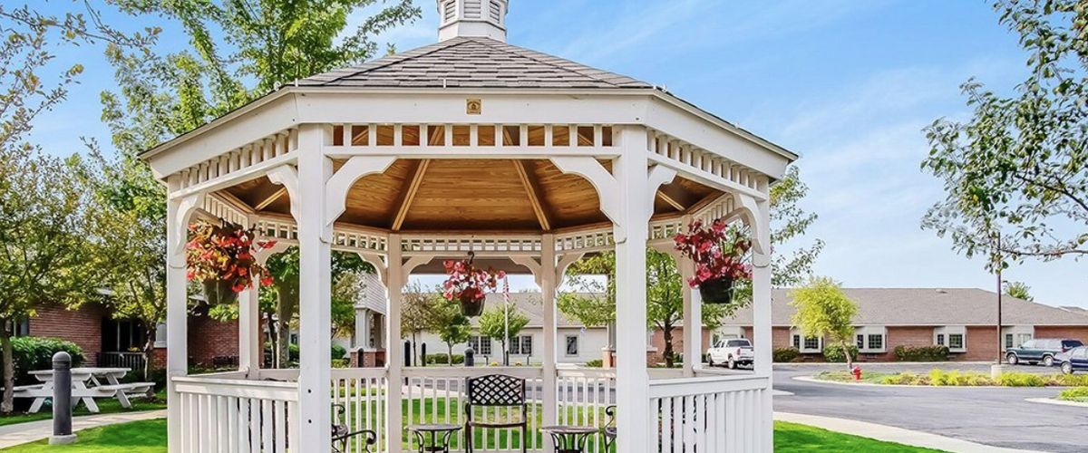 A charming white wooden gazebo with hanging flowers, located in a serene garden setting.